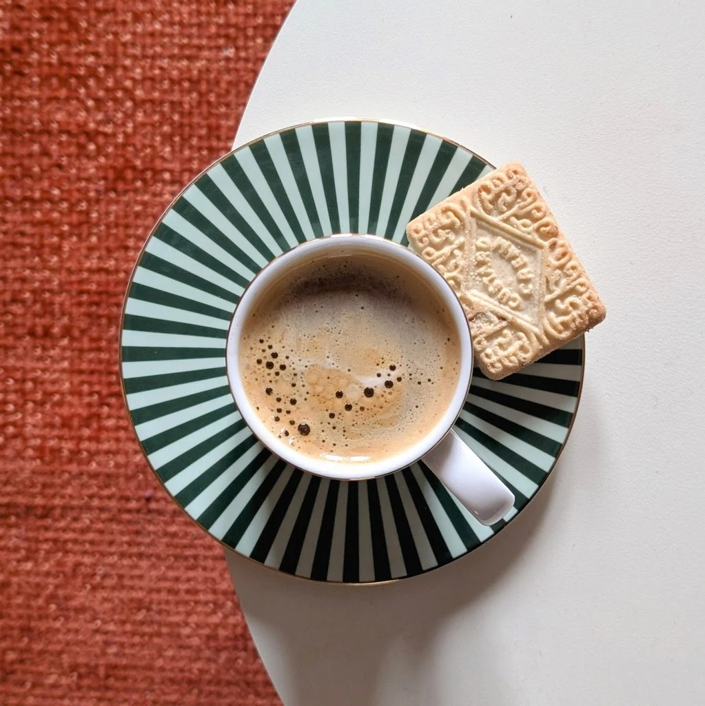 A cup of coffee on a striped saucer with a biscuit