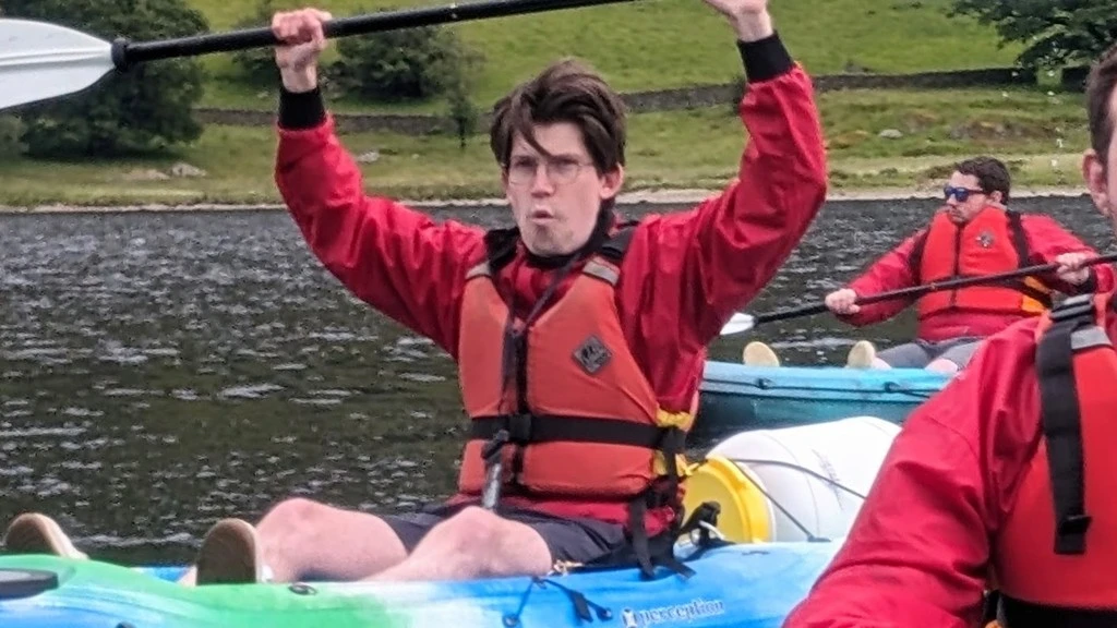 Max kayaking on a lake, paddle raised overhead